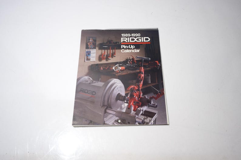 Peut inclure: Un calendrier Pin-Up RIDGID 1989-1990. La couverture pr&eacute;sente une sc&egrave;ne d'atelier avec des outils et des machines. Le calendrier est reli&eacute; en spirale et porte le logo RIDGID. Le fond est blanc.