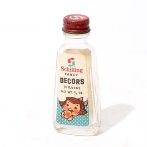 Puede incluir: Una botella de vidrio transparente vintage con tapa de metal roja. La etiqueta dice "Schilling FANCY DECORS (SILVER)" y presenta una niña de dibujos animados. Peso neto 14 gramos.