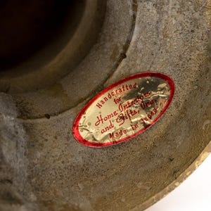 May include: Close-up of a textured, aged brass object. A red and gold oval sticker reads "Handcrafted for Home Interiors and Gifts, Made in Japan."