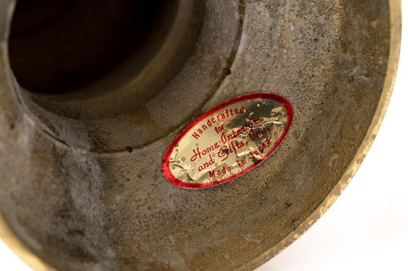 May include: Close-up of a textured, aged brass object. A red and gold oval sticker reads "Handcrafted for Home Interiors and Gifts, Made in Japan."