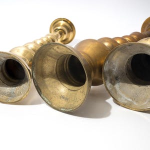 May include: A collection of antique brass candlesticks. The candlesticks have a variety of shapes, including a spiral design and bulbous forms. The brass has a warm, aged patina, and the bases are wide and flared.