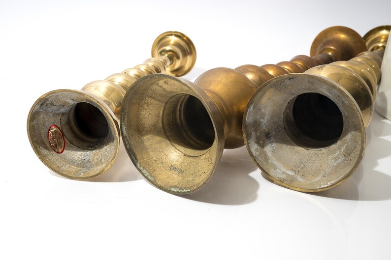 May include: A collection of antique brass candlesticks. The candlesticks have a variety of shapes, including a spiral design and bulbous forms. The brass has a warm, aged patina, and the bases are wide and flared.
