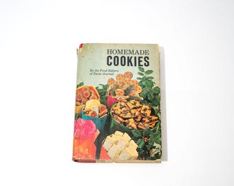 Könnte beinhalten: Vintage Kochbuch mit dem Titel "Homemade Cookies" mit einem farbenfrohen Einband, der verschiedene Kekse und Grünzeug zeigt. Das Buch ist leicht abgenutzt, was darauf hindeutet, dass es gut genutzt wurde. Der Text "By the Food Editors of Farm Journal" ist ebenfalls sichtbar.