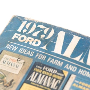 May include: A close-up of the cover of the 1979 Ford Almanac, a blue and white publication with the title "1979 Ford Almanac" and the text "New Ideas for Farm and Home" printed on the cover.