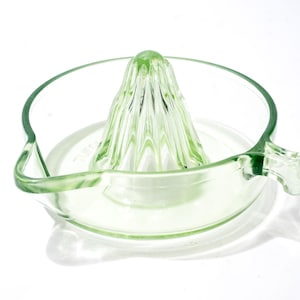 Peut inclure: Presse-agrumes en verre vert clair. Il comprend un cône central et un bol circulaire avec bec verseur et poignée. Le verre translucide présente un design simple et fonctionnel, idéal pour la cuisine.