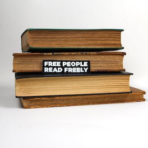 Puede incluir: Una pila de tres libros antiguos de tapa dura con una pegatina negra que dice "FREE PEOPLE READ FREELY" en el segundo libro.