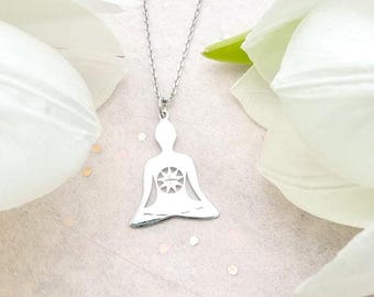 May include: A silver necklace with a pendant shaped like a person in a yoga pose. The pendant has a sun design in the center of the person's chest.