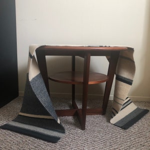 May include: A wooden coffee table with a lower shelf and a white and black striped throw draped over it.