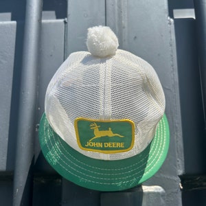 Könnte beinhalten: Weiße Netz-Trucker-Kappe mit einem grünen und gelben John Deere-Logo-Patch und einem weißen Bommel oben.