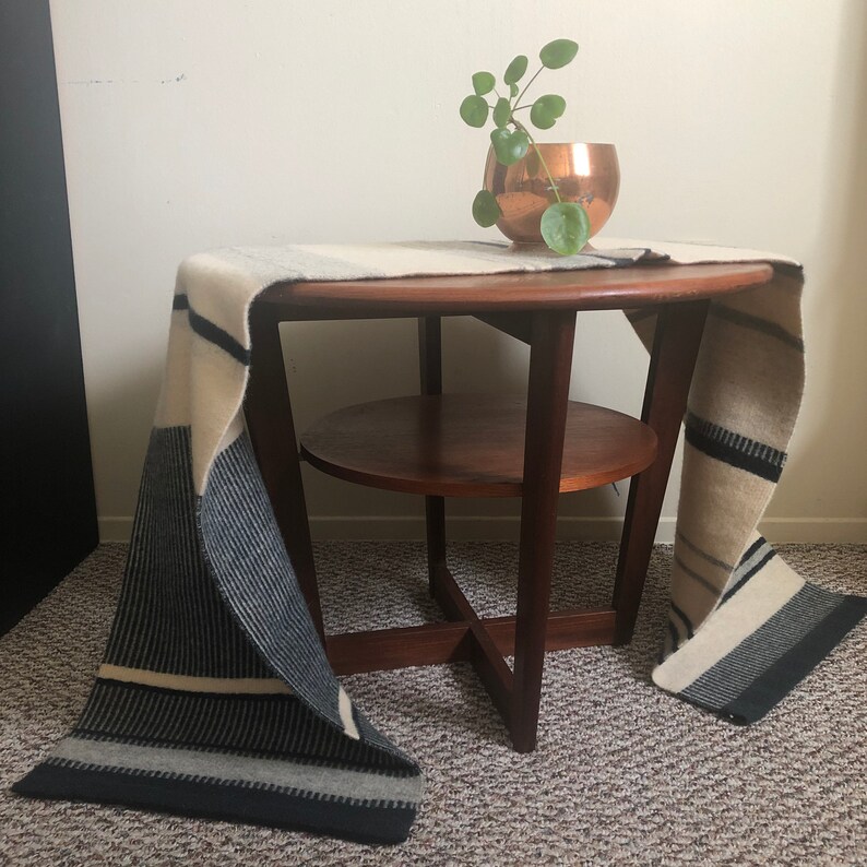 May include: A mid-century modern side table with a lower shelf, made of dark wood. A white and black striped throw blanket is draped over the table.