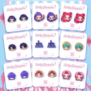 May include: A collection of handmade stud earrings featuring various cartoon character designs. Each pair is displayed on a white card with the text "Sally Shesales GOODY STUDIO HANDMADE IN TEXAS". The earrings showcase diverse hair colors and styles.