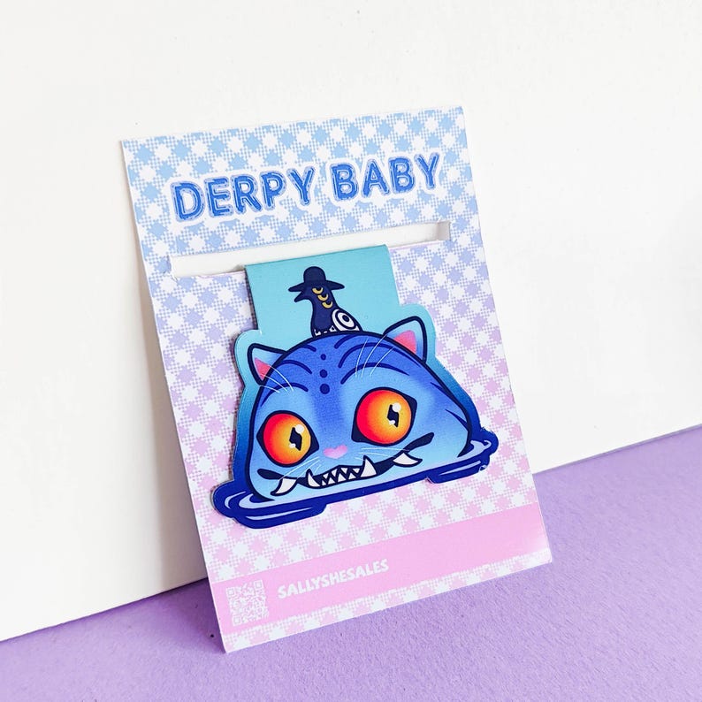 May include: A blue cat-shaped bookmark with orange eyes and a small black hat. The bookmark has the text "DERPY BABY" at the top and "SALLYSHESALES" at the bottom. The background is a light blue and pink gingham pattern.