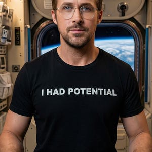 May include: Black crew neck t-shirt with the white text "I HAD POTENTIAL". The person in the image is wearing glasses and is in a space station setting with a view of Earth in the background.
