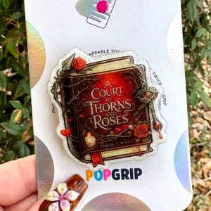 May include: A PopGrip featuring the book cover of "A Court of Thorns and Roses" by Sarah J. Maas. The design includes a red and brown book with roses, thorns, and the book title. The PopGrip is on a white background.