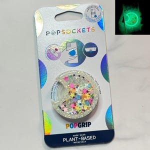 Puede incluir: Un PopGrip PopSockets transparente con confeti colorido en forma de estrella en el interior, empaquetado en una tarjeta holográfica. El embalaje presenta el logotipo de PopSockets e instrucciones. El PopGrip está hecho con materiales de origen vegetal.