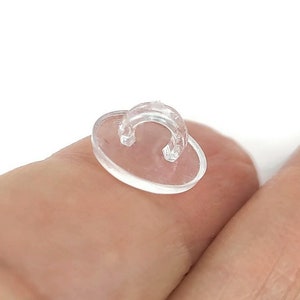 May include: A clear plastic button with a loop on top. The button is designed to be used for attaching items to fabric.