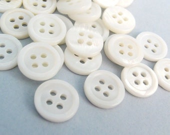 May include: A pile of white, round, four-hole buttons.