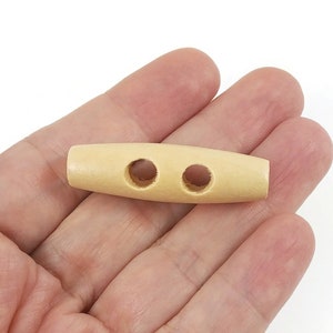 May include: A natural wood toggle button with two holes. The button is oval shaped and has a smooth finish.
