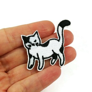 May include: Black and white embroidered iron-on patch of a cat with a black tail.