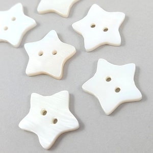 May include: Six white star-shaped buttons with two holes each. The buttons are made of mother of pearl and have a smooth, polished finish.