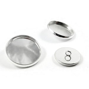 May include: Three silver-toned metal round button blanks. The blanks are different sizes and have a smooth, shiny finish.