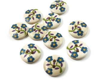 May include: Ten wooden buttons with a floral design. The buttons are cream colored with blue and purple flowers and green leaves.