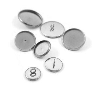 May include: A set of silver-toned metal round cabochon settings with a variety of sizes. Some of the settings have a loop on the back.