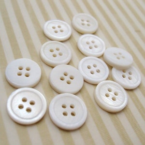 May include: A collection of white pearl buttons with four holes each. The buttons are arranged in a semi-circle on a striped background.