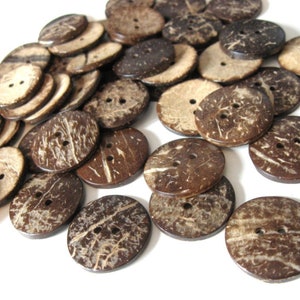 May include: A collection of round, natural coconut shell buttons in various shades of brown. Each button has two or four holes for sewing. The buttons have a textured surface and are scattered across a white background.