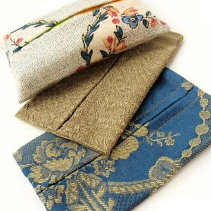 May include: Three fabric tissue box covers. The top cover is white with a floral pattern in shades of pink, green, and blue. The middle cover is brown with a subtle texture. The bottom cover is blue with a gold floral pattern.