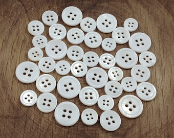 May include: A collection of white pearl buttons of various sizes, arranged in a circular pattern on a wooden surface.