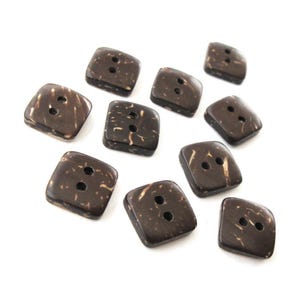 May include: A collection of ten square, dark brown buttons with two holes each. The buttons have a natural, speckled appearance with lighter brown markings. The buttons are made of a natural material and are arranged on a white background.