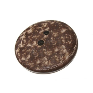 May include: A brown coconut shell button with two holes. The button has a natural, marbled pattern.