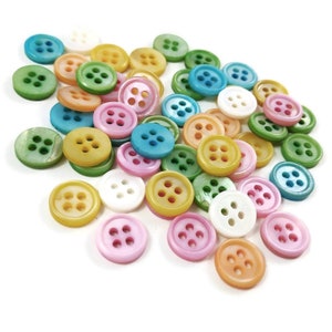 May include: A collection of colorful, round, plastic buttons with four holes each. The buttons are in various shades of blue, green, pink, yellow, and white.