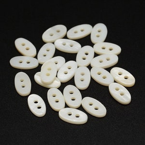 May include: A collection of white oval-shaped buttons with two holes each. The buttons are made of mother of pearl and have a smooth, glossy finish.