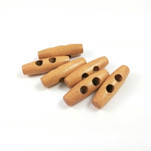 May include: A collection of light brown wooden toggle buttons. Each button is cylindrical with two holes for sewing. The buttons are arranged on a white surface, showcasing their natural wood grain and simple design.