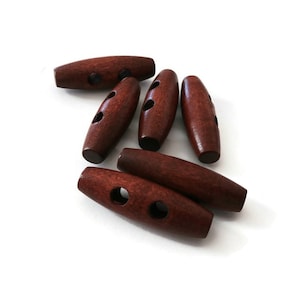 May include: Six brown wooden toggle buttons with two holes each. The buttons are oval shaped and have a smooth finish.