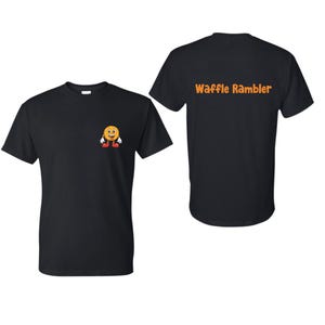 Puede incluir: Camiseta negra con un gr&aacute;fico de waffle amarillo sonriente en la parte delantera y el texto "Waffle Rambler" en la parte posterior.