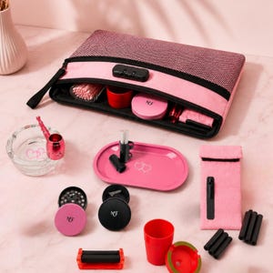 Könnte beinhalten: Eine rosa-schwarze Aufbewahrungstasche mit Reißverschluss und Zahlenschloss, die verschiedene Zubehörteile enthält, darunter einen klaren Glasaschenbecher, eine rosa Metallpfeife, ein rosa Drehtablett, einen rosa Grinder, eine rosa Tasche und Behälter.