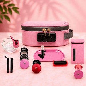 May include: A pink smell-proof storage bag with a black combination lock, accompanied by a glass ashtray, a pink metal pipe, a pink rolling tray, a black rolling machine, a pink grinder, two black tubes, a pink pouch, and a pink metal cup.