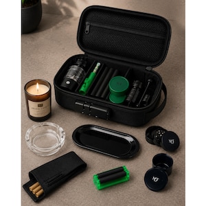 May include: A black zippered storage case with a combination lock containing various accessories, including a green rolling tool, black tubes, and containers. Nearby are a glass candle, a clear glass ashtray, a black tray, and a black pouch.