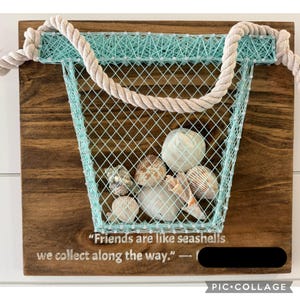May include: Wooden wall art featuring a string art basket in light blue, filled with seashells. The basket is attached to a brown wooden board with a rope handle. Text reads: "Friends are like seashells we collect along the way."