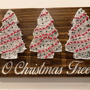 May include: Wooden Christmas sign featuring three string art Christmas trees with white string, red accents, and green dots. The sign reads "O Christmas Tree" in white script, perfect for holiday decor.