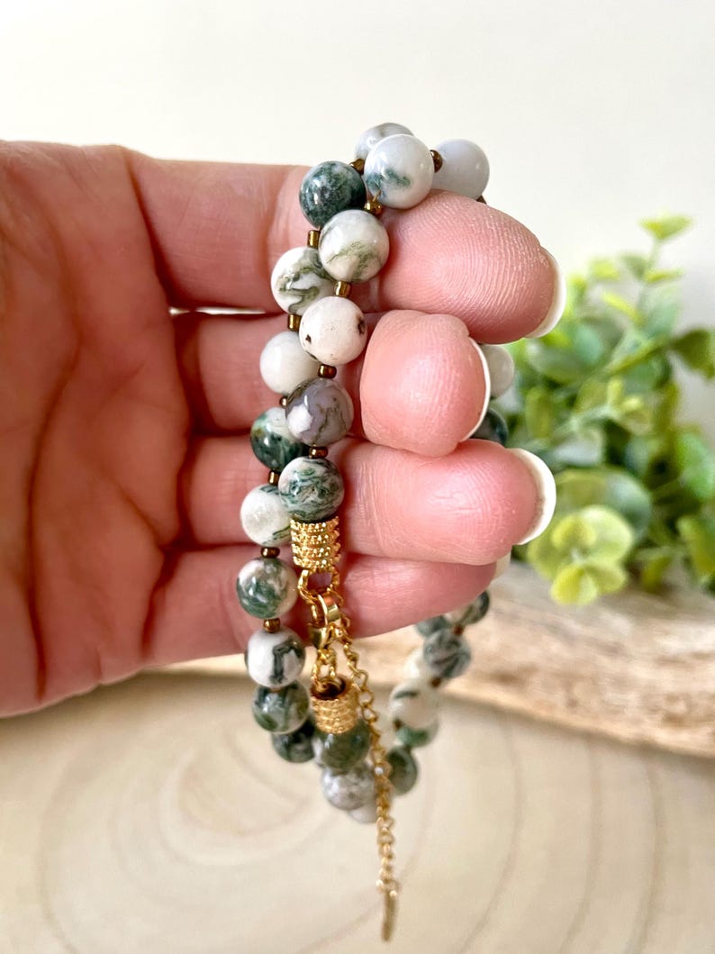 May include: A double-strand bracelet featuring round beads in shades of white, green, and gray. The beads are strung together with gold-colored accents and a delicate chain.