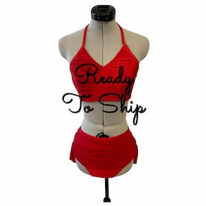 May include: A bright red two-piece bikini set displayed on a mannequin. The top features a halter neckline with a wrap-style front, while the high-waisted bottoms have gathered side details. The text Ready To Ship is overlaid in black script.