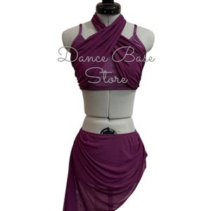 May include: A deep purple two-piece dance outfit featuring a crisscross halter top with thin straps and a matching asymmetrical mesh skirt. The text 'Dance Base Store' is printed in white across the center of the top piece of the garment.