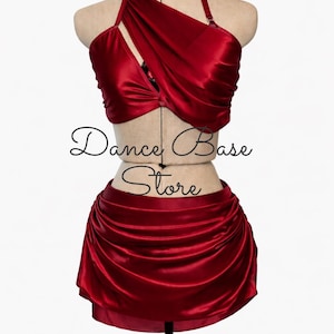May include: A two-piece set in deep red satin featuring a halter-style top with draped fabric across the chest and a matching mini skirt with gathered side detailing. The text Dance Base Store is overlaid across the center of the garment.