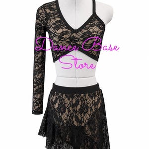 May include: A black lace two-piece dance outfit on a mannequin featuring a long-sleeved asymmetrical crop top with a V-neckline and a matching skirt with a ruffled hem. The text "Dance Base Store" is overlaid in pink across the center of the garment.
