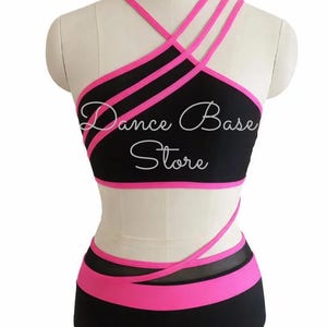 May include: A black and hot pink two-piece dance outfit featuring a crop top with multiple thin straps and a high-waisted bottom with a matching pink waistband. The text Dance Base Store is printed in white across the center of the crop top.
