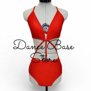 May include: A bright red leotard featuring a deep V-neckline, thin straps, and a cutout midsection with crisscross detailing. The garment is displayed on a mannequin and includes the black text overlay Dance Base Store across the center.